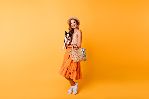 Fulllength portrait of romantic young lady with summer hat holding dog Stunning redhaired girl in long skirt posing with french bulldog