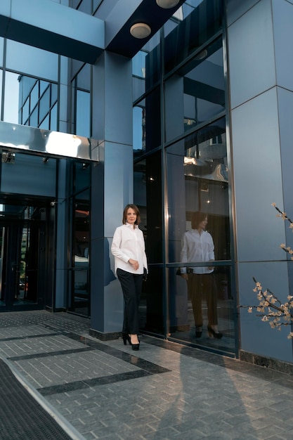 Fulllength portrait of young business woman in formal attire against the backdrop of modern building with glass facade