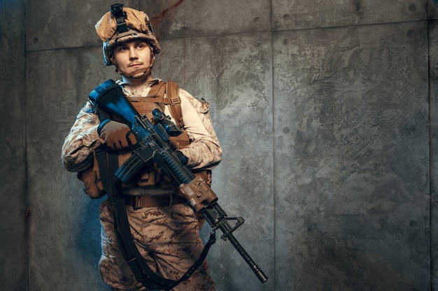 Fully equipped army soldier in camo uniform and helmet, armed with pistol and assault service rifle