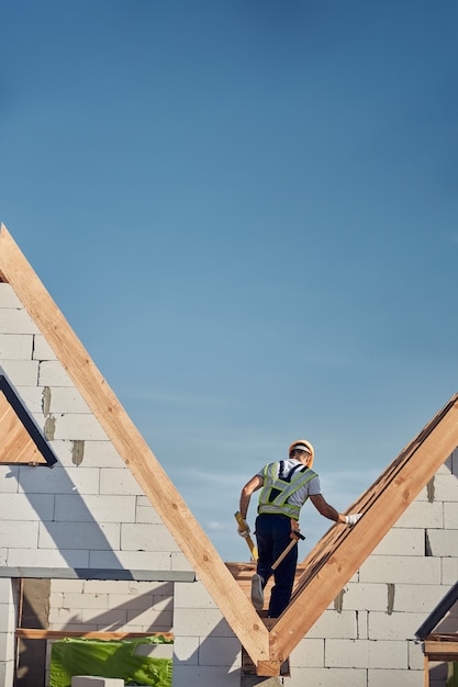 Foto lavoratore in altezza completamente equipaggiato in piedi tra i tetti delle case di mattoni