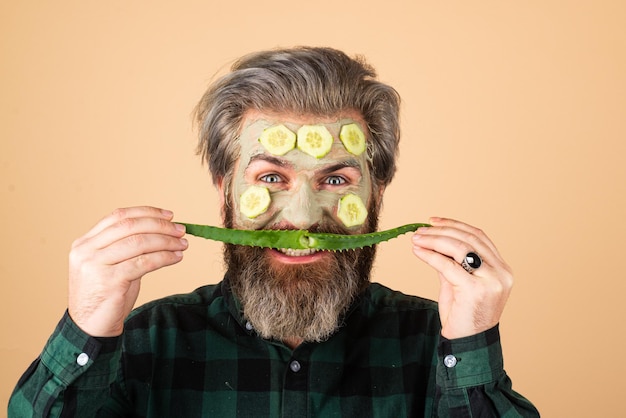 Fun aloe vera moustache. Funny man model with clay mask and cucumber slices on face. Spa, dermatology, wellness and facial treatment concept. Male face care.