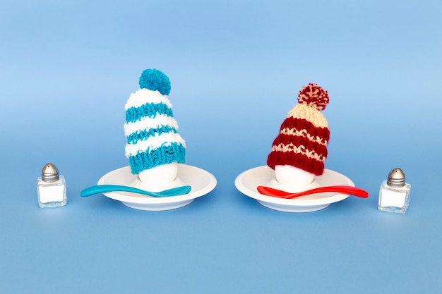 Photo fun breakfast concept with boiled eggs wearing knitted woolen hats on blue background