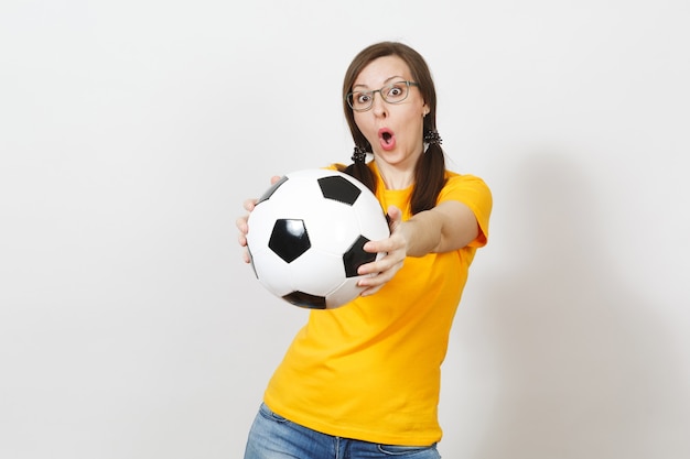 Fun cheerful european woman, two pony tails, football fan or\
player in glasses, yellow uniform hold classic soccer ball isolated\
on white background. sport, play, football, healthy lifestyle\
concept.