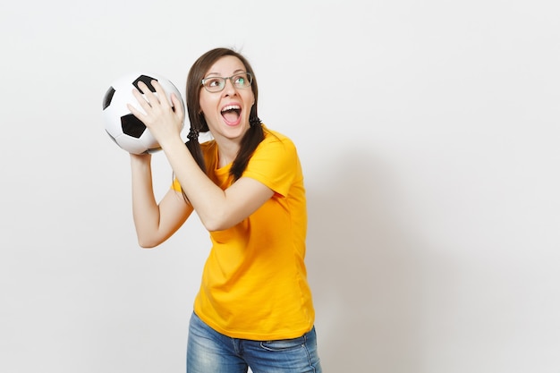 Fun cheerful european woman, two pony tails, football fan or\
player in glasses, yellow uniform hold classic soccer ball isolated\
on white background. sport, play, football, healthy lifestyle\
concept.