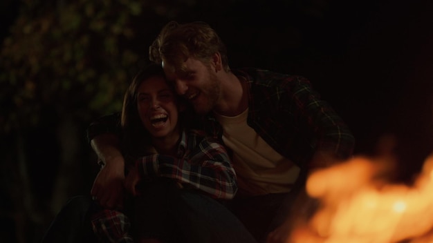 Fun couple laugh together on night camp site Close up smiling millennials have fun on romantic date Lovely family hug cuddle by bonfire Joyful lovers travel hike outdoors Happiness leisure concept