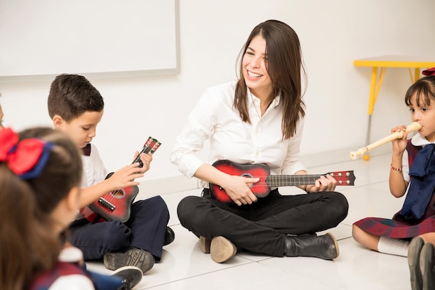 Foto insegnante prescolare femminile divertente che suona una chitarra e insegna un po' di musica ai suoi studenti