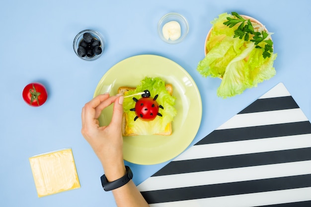 Fun food art for kids. Ladybug sandwich on blue wall. How to make creative breakfast for kid at home. Step by step instruction, view from above.