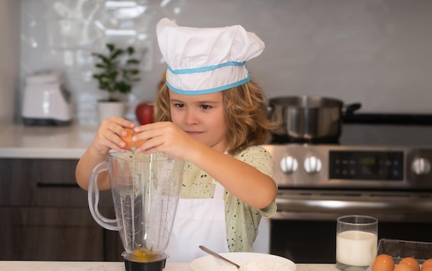 Fun kids kitchen Funny little kid chef cook wearing uniform cook cap and apron cooked food in the kitchen Kids are preparing food bake cookies in the kitchen