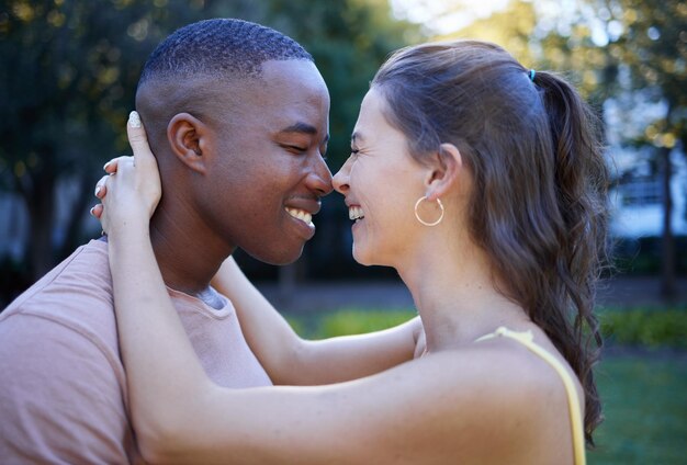 Fun love and interracial couple at park for date summer holiday and outdoor wellness with hug care and nose game Happy young and diversity people in green garden nature and excited together