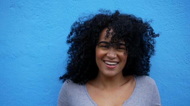 Photo a fun loving young woman leaning on blue wall laughing and smiling