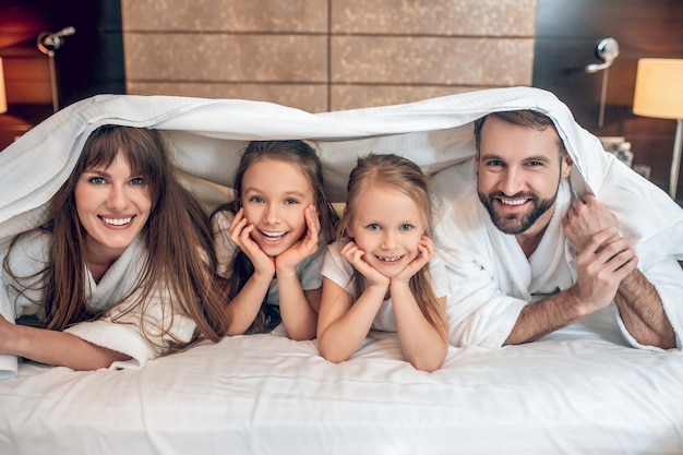 Fun. Smiling family in white robes lying in bed and having fun