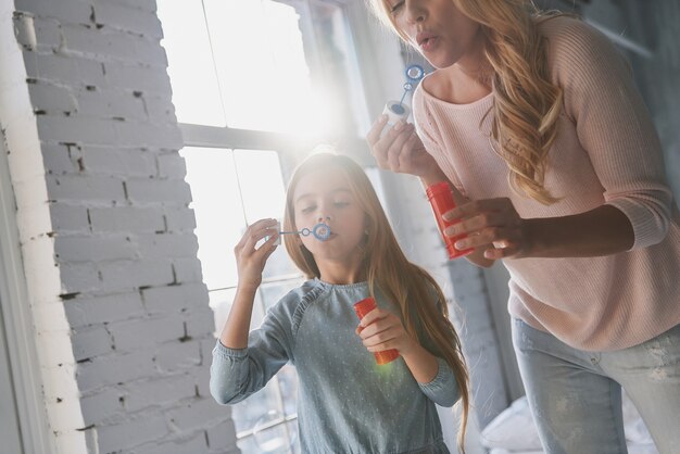 Tempo di divertimento. madre e figlia che soffiano bolle di sapone mentre trascorrono del tempo a casa