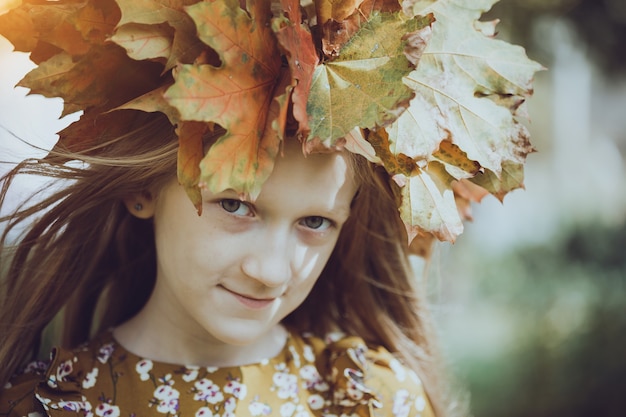 Fun young girl at the park with diadem from yellow maple leaves