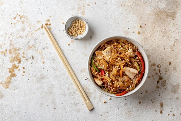 Photo funchose salad with chicken and vegetables in bowl with wooden chopsticks on textured background top view with text space asian food menu