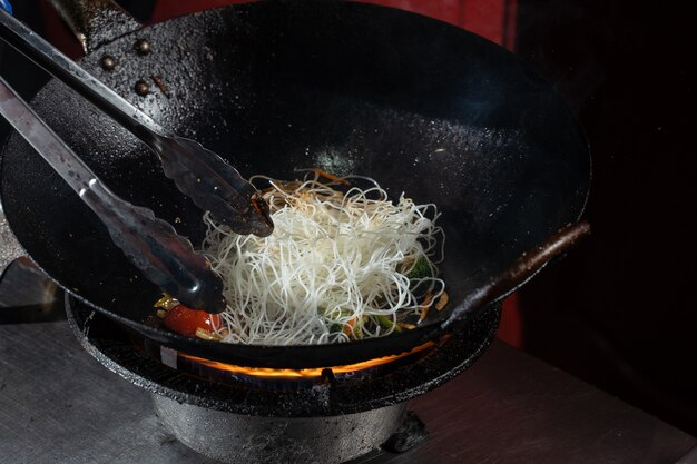 Funchoza flambe rice noodles with vegetables cooking on fire in wok pan. Street food.