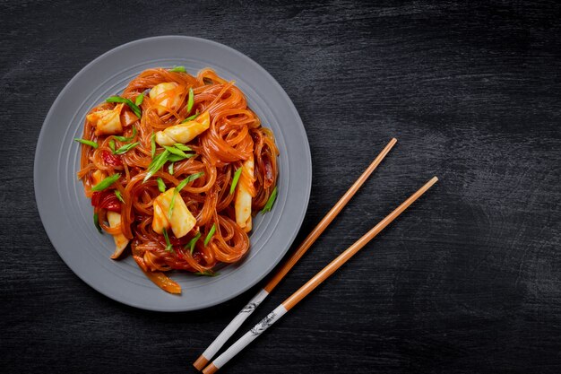 Funchoza with squid and vegetables on a black background, top view, copy space. Glass noodles, Asian food. 