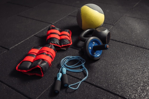 Functional training equipment. Kettlebell and skipping rope, ab roller, medicine ball, massage roller, weights on a dark black floor. Bodybuilding and fitness