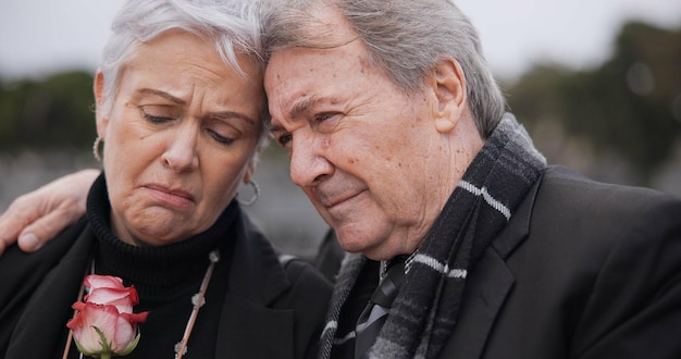 Funeral graveyard and senior couple hug for comfort empathy and support at memorial service Depression grief and sad man and woman embrace with flower for goodbye mourning and burial for death