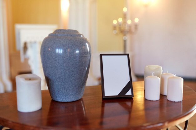 Photo funeral and mourning concept - photo frame with black ribbon, cremation urn and candles on table in church