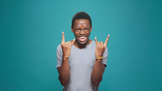 Funky uomo cool che mostra il segno del rock metal con le mani davanti alla telecamera, esprimendo musica punk divertente con energia positiva. maschio hipster rocker che gesturing le corna del diavolo simbolo per l'intrattenimento.