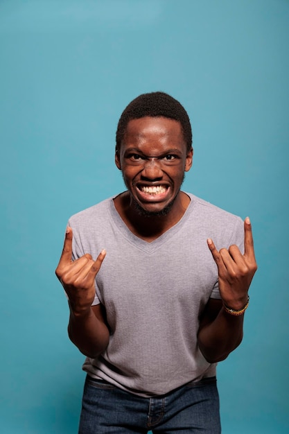 Funky man advertising rock and roll gesture with fingers in front of camera, expressing love for heavy metal music. Confident adult feeling excited about rock gesture to show cool sign.