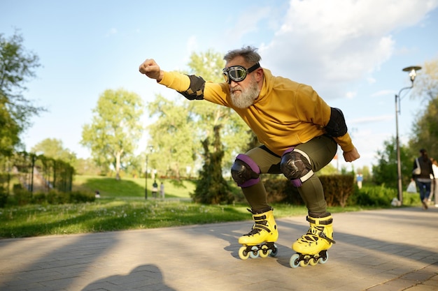 Funky mature man wearing goggles riding like aviator moving fast on roller skates in city street