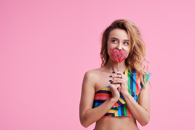 La signora attraente allegra positiva funky con i suoi capelli ricci dell'onda alla moda alla moda, tiene una ventosa dello zucchero sul bastone isolato sul rosa