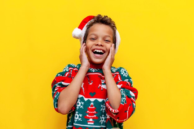 Funny african american boy in christmas clothes smiling on yellow isolated background