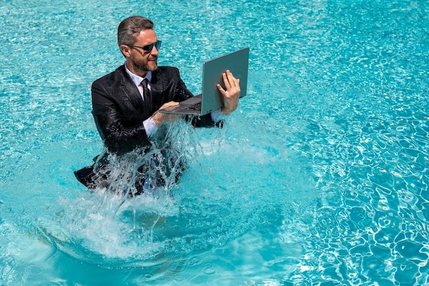 Funny amazed businessman in suit with laptop in swimming pool crazy excited business man on summer v