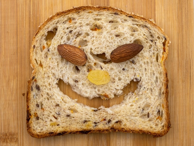 Фото Забавная мордочка животного из ломтика мультизернового хлеба, миндаля и изюма. радостная здоровая пища на деревянном фоне.
