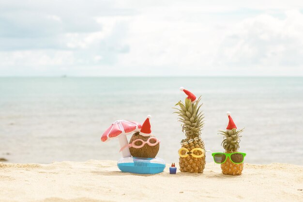 Funny attractive pineapple and coconut in stylish sunglasses on the sand against turquoise sea