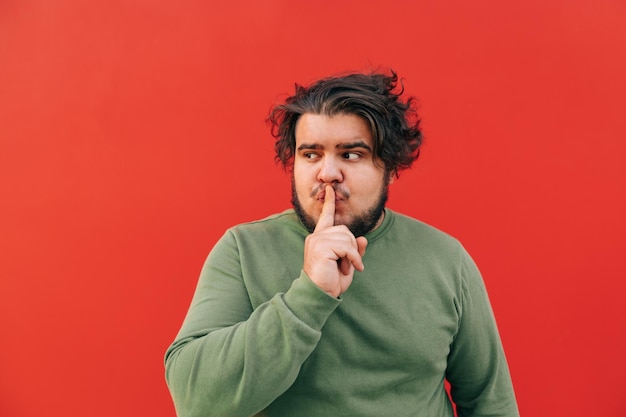 Funny attractive young bearded hispanic man is showing a shh gesture by touching his mouth