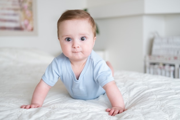 Funny baby boy 6 months old in blu bodysuit smiling and lying on bed at home
