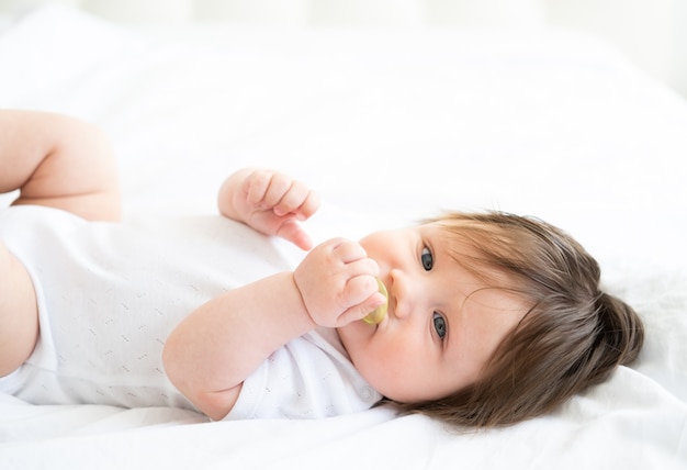 Funny baby boy  month with nipple lying on a white bedding at home