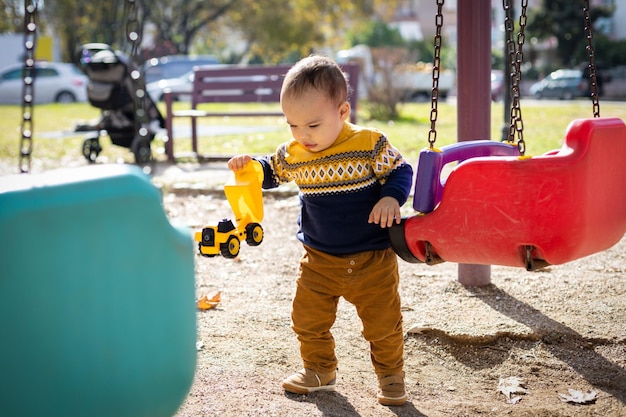 Bambino divertente che gioca al parco giochi all'aperto il bambino gioca con l'auto giocattolo bella giornata di sole