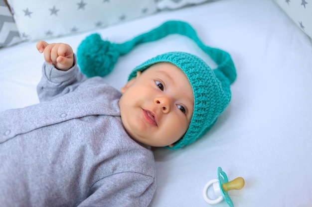 A funny baby in a funny hat lies in the crib