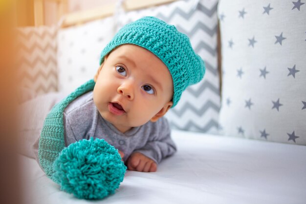 A funny baby in a funny hat lies on his stomach with his head raised