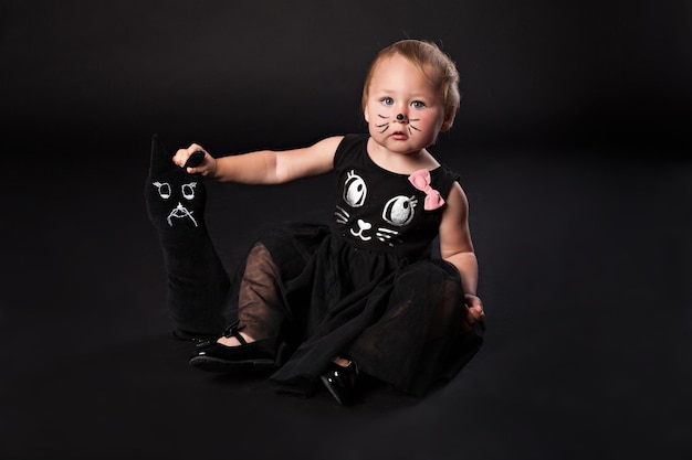 Funny baby girl in cat costume against black background