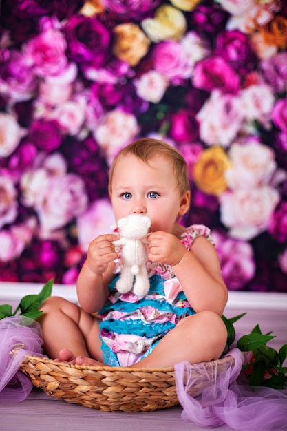 Photo funny baby girl toddler sitting in basket on flower decoration in studio and kissind teddy bar