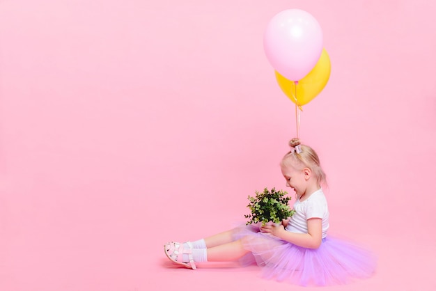 Funny baby girl in white t-shirt and lilac skirt with balloons on pink background. Children's portrait with space for text.