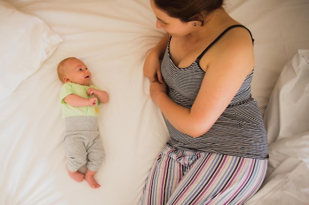 The funny baby is lying on the bed and looking at his mother with pleasure