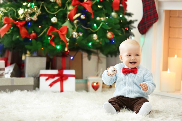 Funny baby sitting on soft carpet, on Christmas interior background