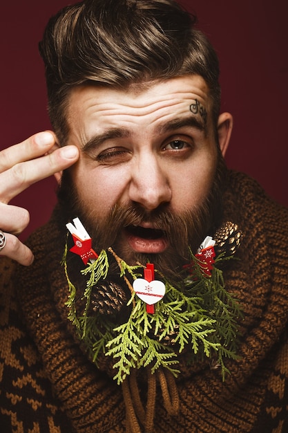 Photo funny bearded man in a new year's image as santa claus with decorations on his beard. feast of christmas.