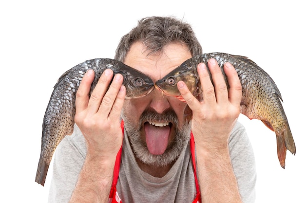 Funny bearded merchant or cook holding raw freshwater fish at eye level and showing tongue