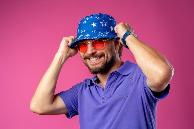 Photo funny bearded smiley man wearing beach hat and sunglasses against pink