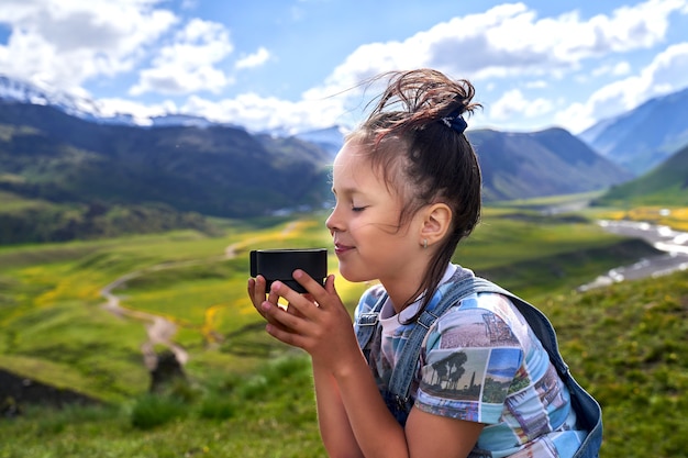 Funny beautiful girl holds a mug and drinks tea in the mountains.