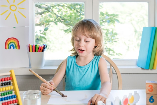 Funny beautiful happy child boy draws laughing with paint selective focus