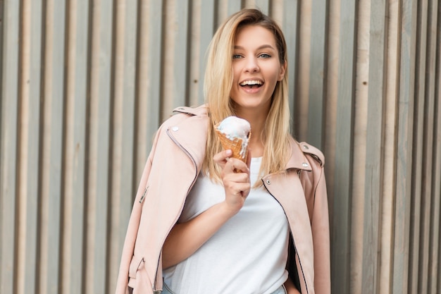 Funny beautiful woman with smile in a trendy pink jacket holds an ice cream near