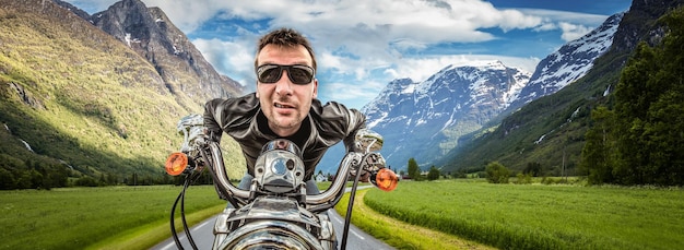 Foto divertente motociclista in occhiali da sole e giacca di pelle che corre sulla serpentina di montagna. filtro applicato in post-produzione.