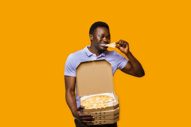 Funny black courier eats piece of pizza and holds 4 pizza boxes